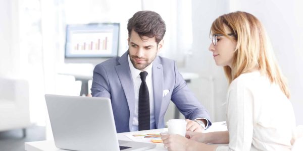 Portrait of young bank officer consulting with businesswoman while sitting at office in front of laptop.