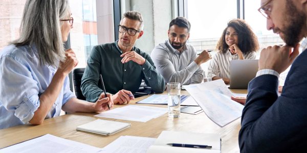 Diverse international executive business partners group discuss report at boardroom meeting table. Multiracial team negotiating project developing business strategy doing paperwork analysis in office.